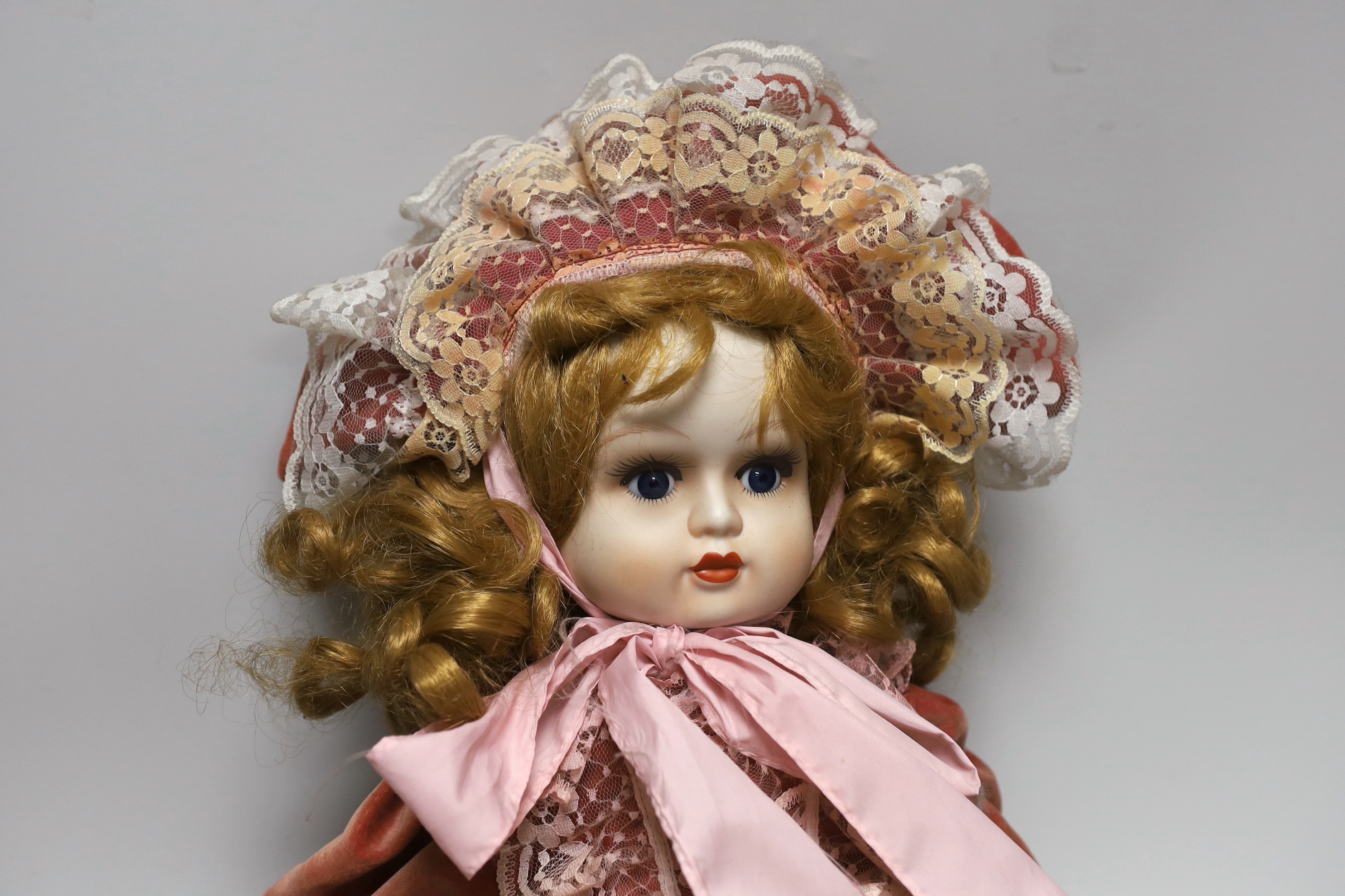 A doll with bisque face and hands, wearing a velvet dress and bonnet, 66cm high